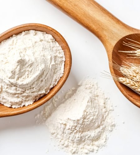 A close-up shot of two wooden spoons, one filled with flour and the other with wheat ears, on a white background. The image is perfect for showcasing baking ingredients, traditional food, or the process of making bread.